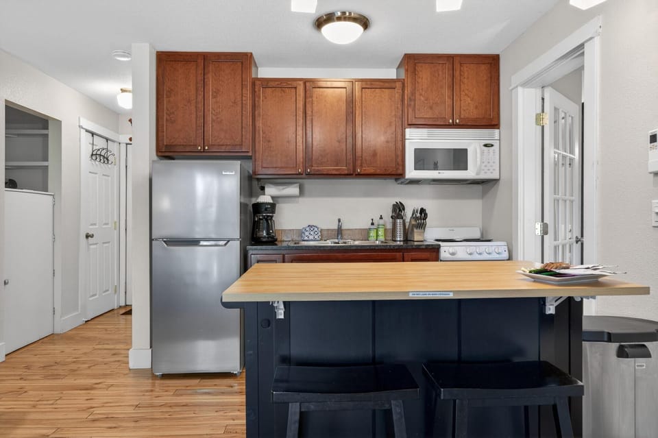 Kitchen features stainless steel fridge, dark granite countertop, warm wood cabinets, and a light wood breakfast bar.