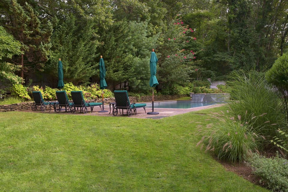 Brick patio with 4 lounge chairs, 2 tables and 3 sun umbrellas.