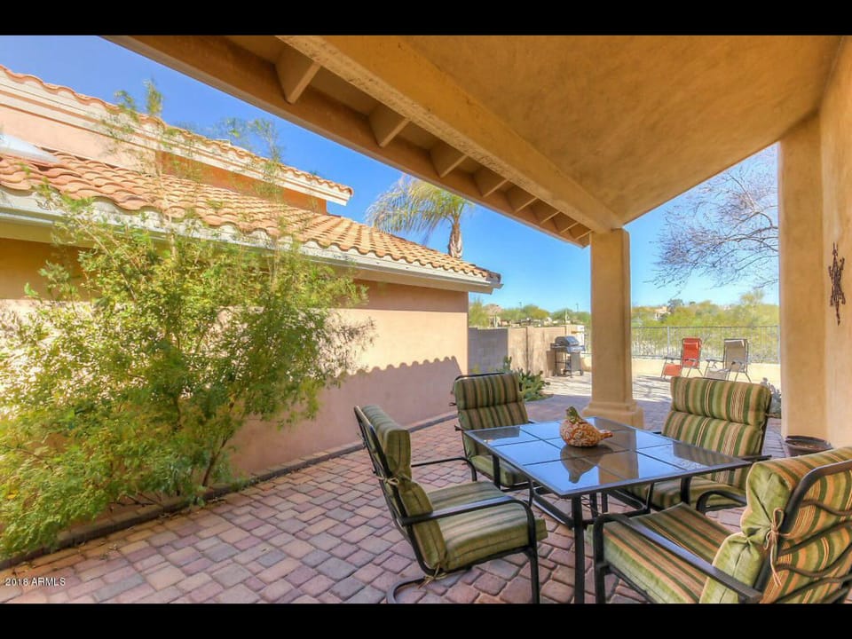 Covered patio area with table and chairs and gas grill