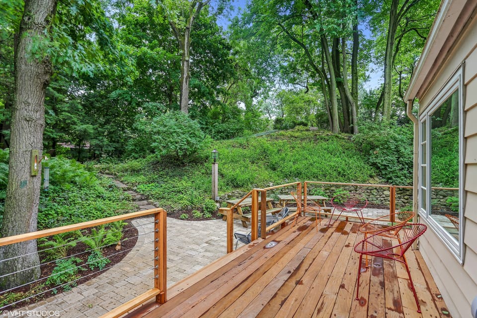 Deck with view of wooded yard and fire pit with 8 chairs and path to parking