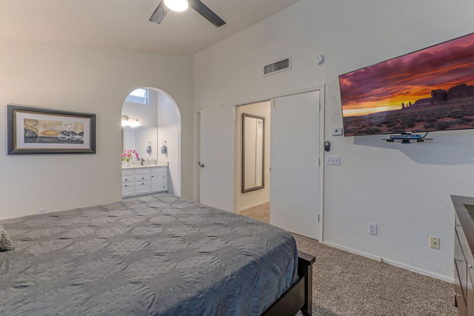 Spacious upstairs primary bedroom features a king bed, ceiling fan, walk-in closet, large TV and en suite bath.