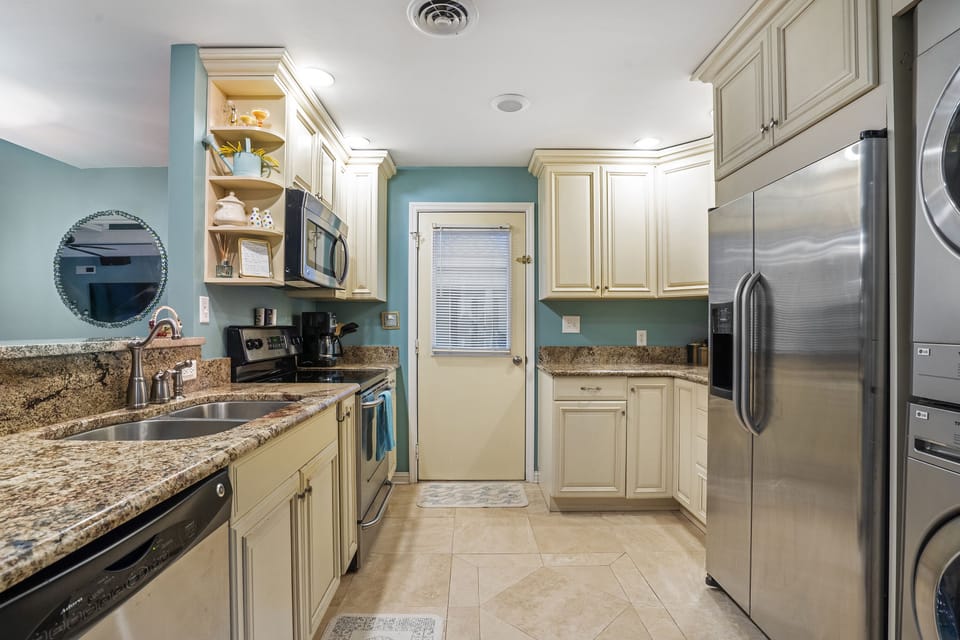 Full kitchen view. Stainless steel refrigerator, full sized stacked washer/dryer