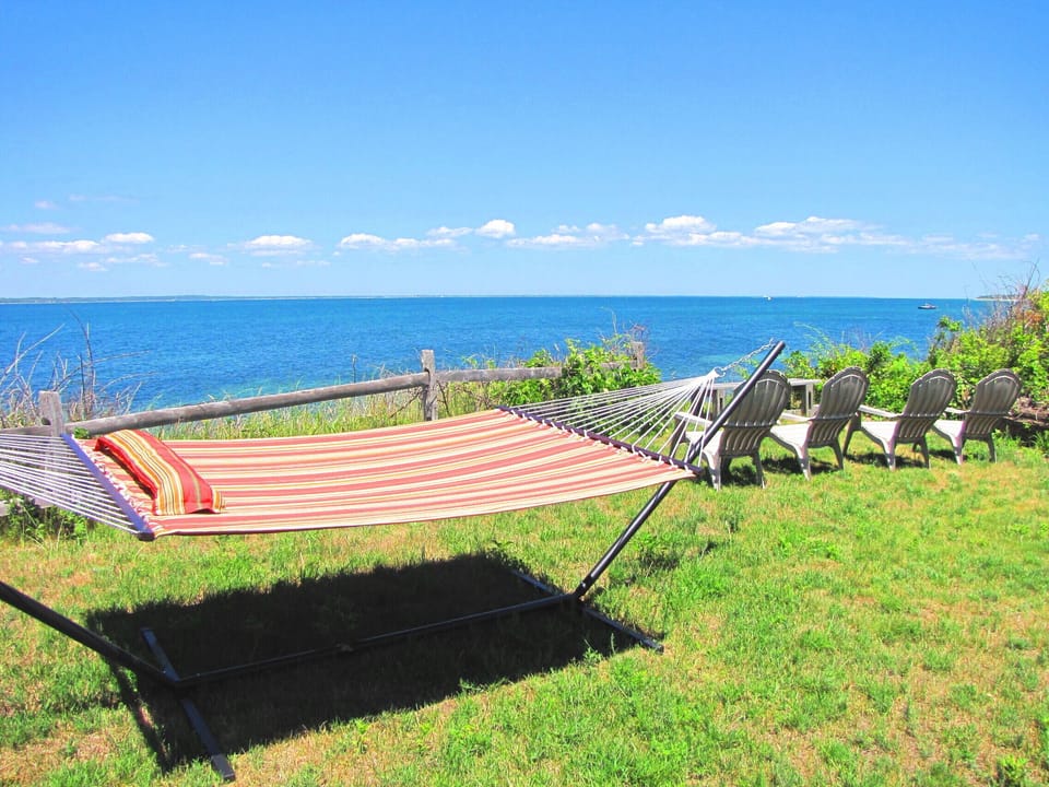 Large grassy yard overlooking ocean with a bench , hammock & 4 adirondack chairs