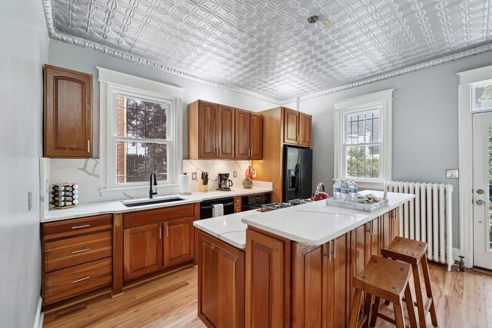 Elegant kitchen with warm wood cabinetry, tin ceiling, and bright natural light.