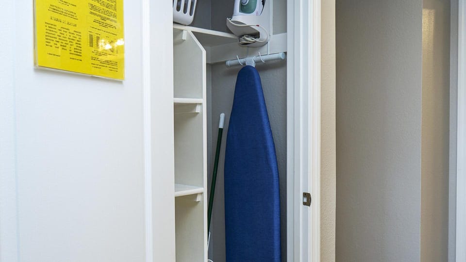 Utility closet furnished with Iron, Ironing Board, Laundry basket and more.