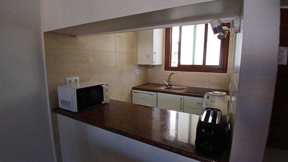 Kitchen with kettle, toaster, microwave, air fryer, fridge, hob and sink.