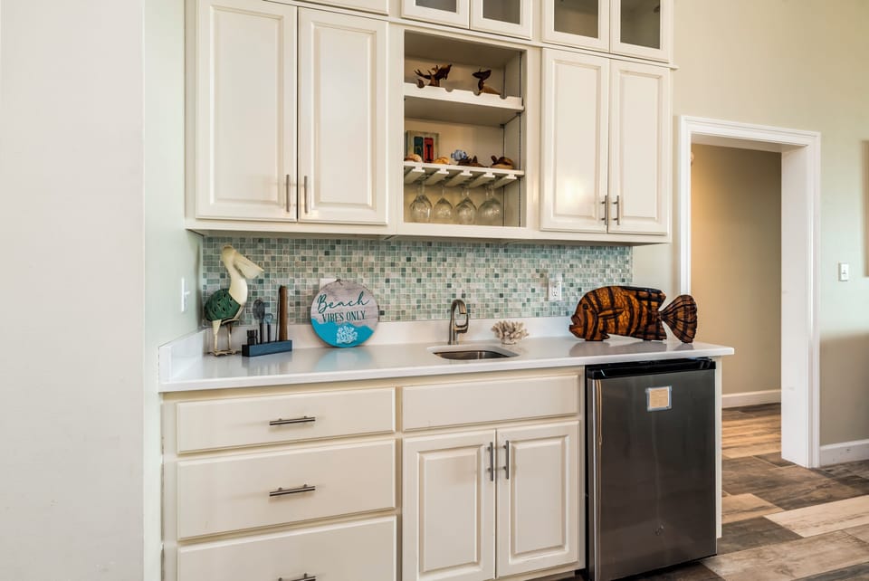Your kitchen features white cabinetry, mosaic backsplash, and wine storage—perfect for preparing meals and beach-themed entertaining.