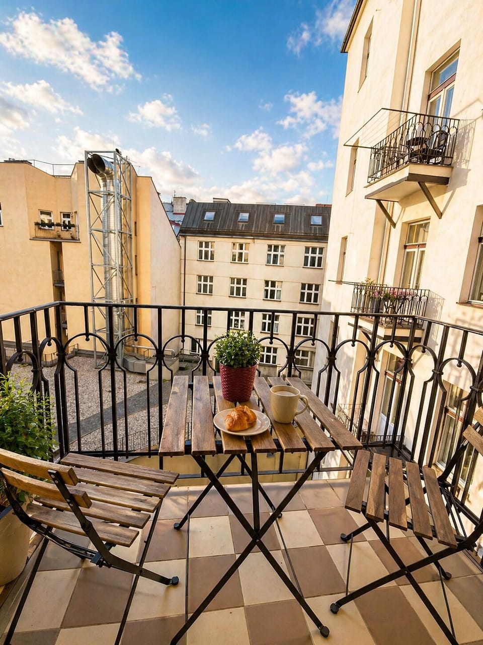 Sunny balcony with breakfast setup, courtyard view, and charming seating.