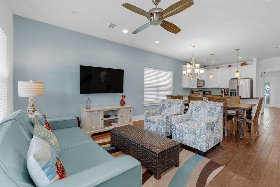 Living space with seating and wood floors, flowing to dining area & kitchen