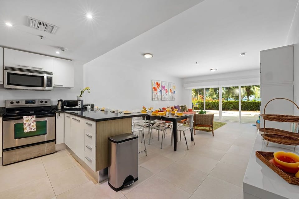 Your bright, modern kitchen flows seamlessly into the dining area, where sunlight pours through sliding doors overlooking lush tropical palms—perfect for morning coffee or prepping vacation meals.