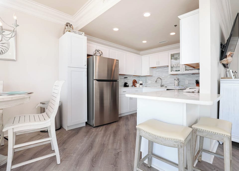 Bright and airy kitchen area features white cabinetry, a breakfast bar with seating, and modern stainless appliances