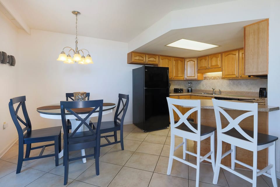 Kitchen featuring light wood cabinetry, a black refrigerator, and the dining area with a round table and blue chairs