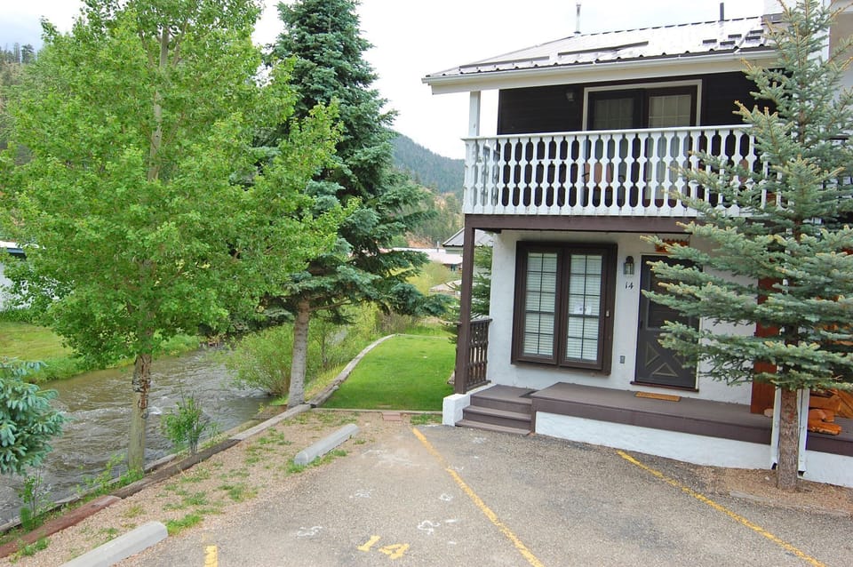 Two-level mountain property featuring alpine architecture, convenient parking, and a decorative balcony, surrounded by evergreen trees and landscaped grounds in a peaceful mountain setting.