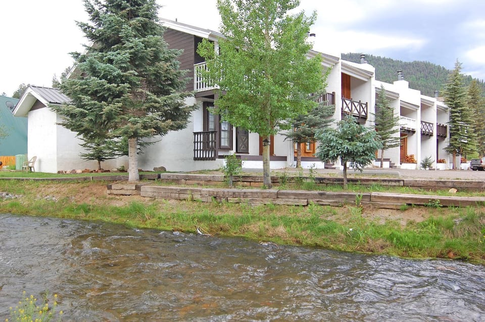 A mountain village retreat with balconies overlooking a gentle stream, surrounded by evergreens and peaceful natural scenery.