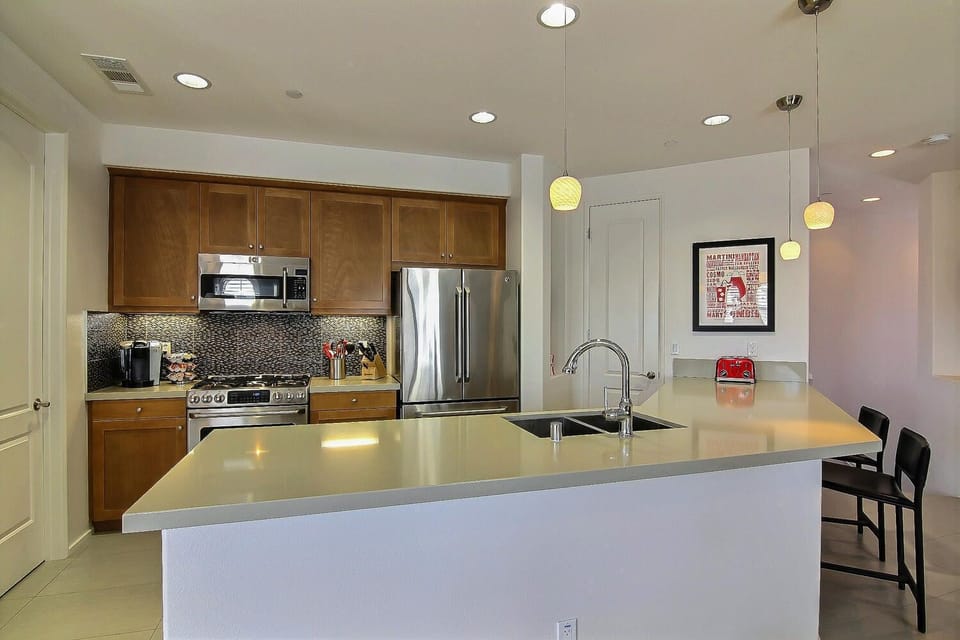 Open kitchen with 'Caesarstone' island/countertop and tile backsplash.