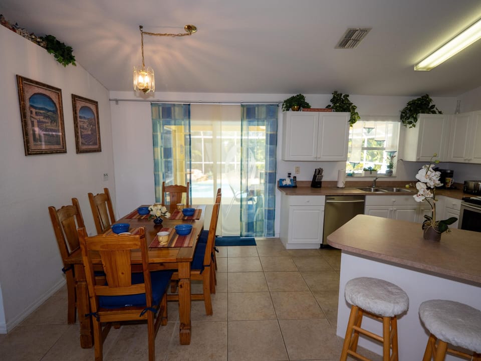 Dining area with wooden table, six chairs with blue cushions, and sliding glass door to pool patio.
