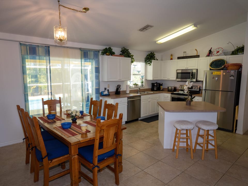 Dining area features a wooden table with six chairs and blue cushions beside sliding doors with blue-striped curtains.