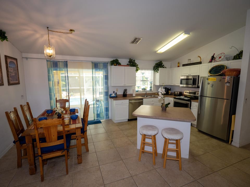 Kitchen and dining area with white cabinetry, stainless steel appliances, wooden table set for six, and sliding glass doors.