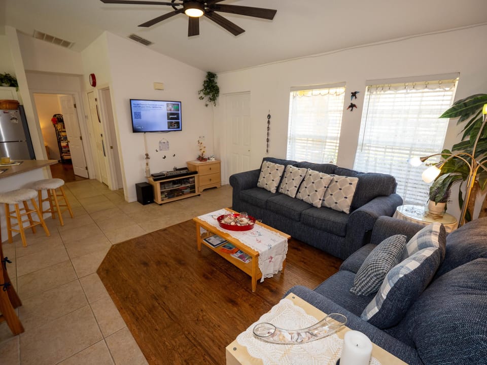 Living room features two blue fabric sofas with patterned pillows, a wood coffee table, and a wall-mounted TV.