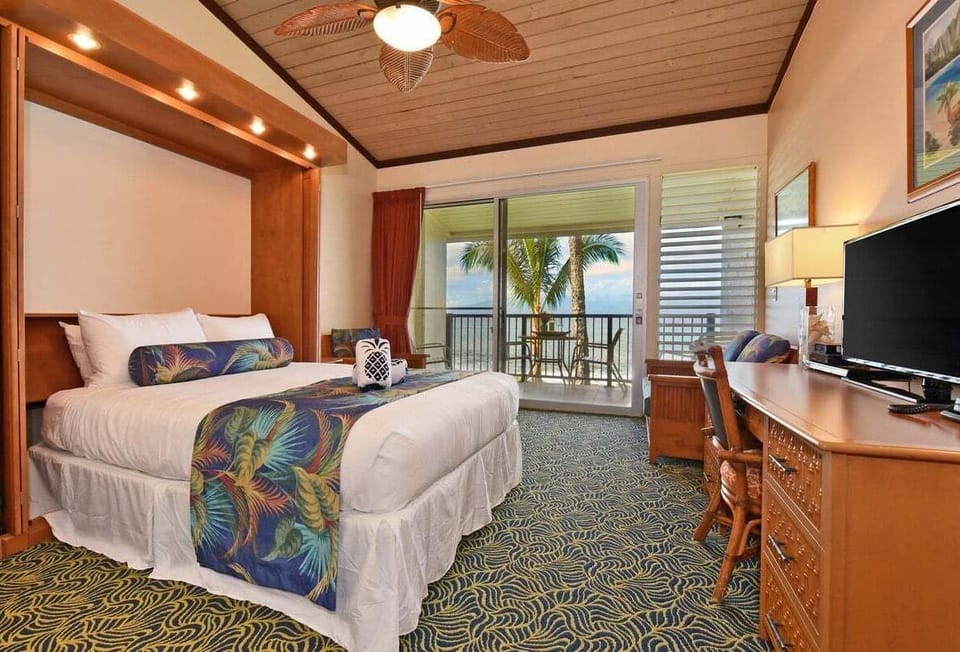 Bright twin bedroom with balcony access — tropical bedding, ceiling fan, and workspace for comfort and function.