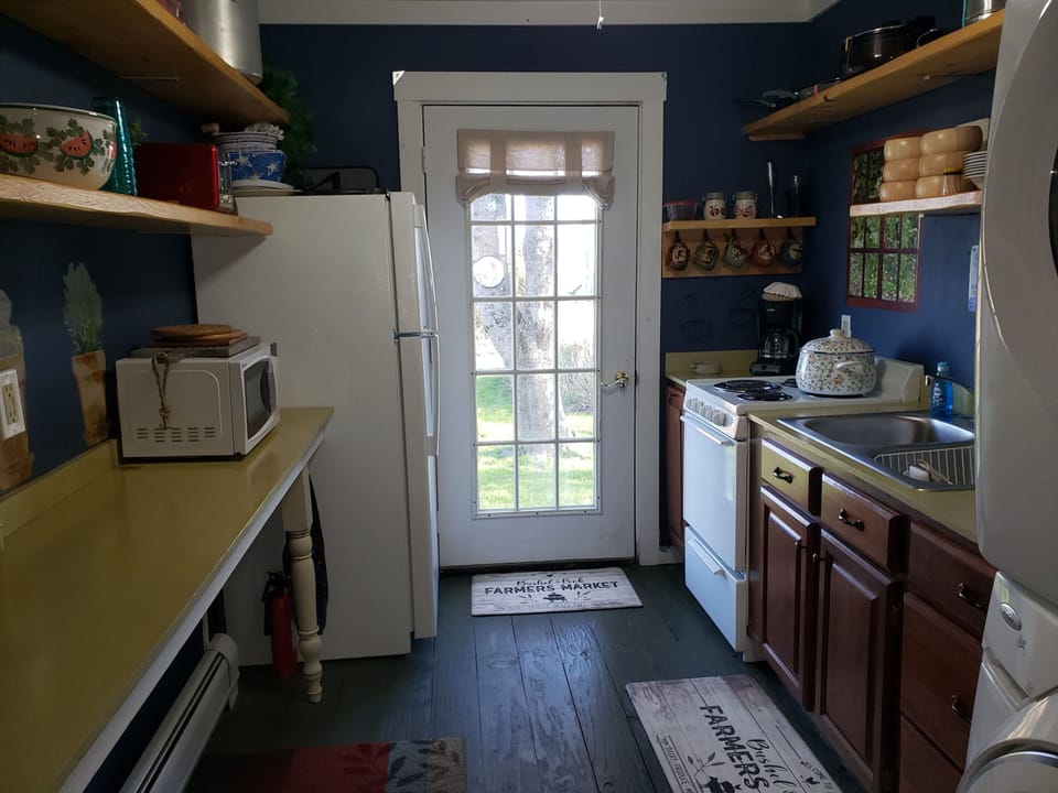 View of open shelving galley kitchen. Door to side yard with picnic bench.