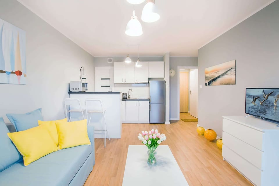 A bright living room with a comfortable blue and yellow sofa, a wooden coffee table, and a small dining area in the background, creating a cozy and welcoming atmosphere.