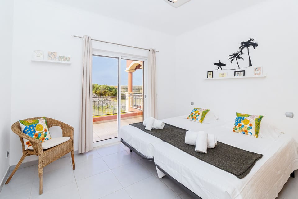 Bright twin bedroom with balcony access and wicker chair — Villa Farol, holiday villa in Vila do Bispo