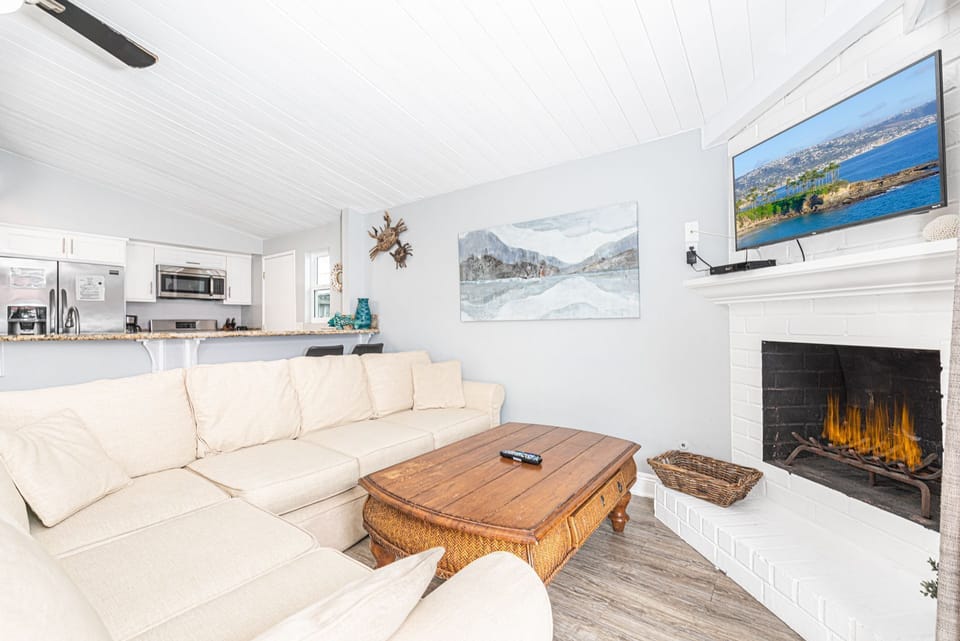 The living area includes sofa, cable TV, dining table with seating for 6, and kitchen beyond.
                