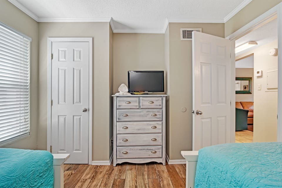 Flat screen tv, clothing drawers and closet in twin bedroom.
