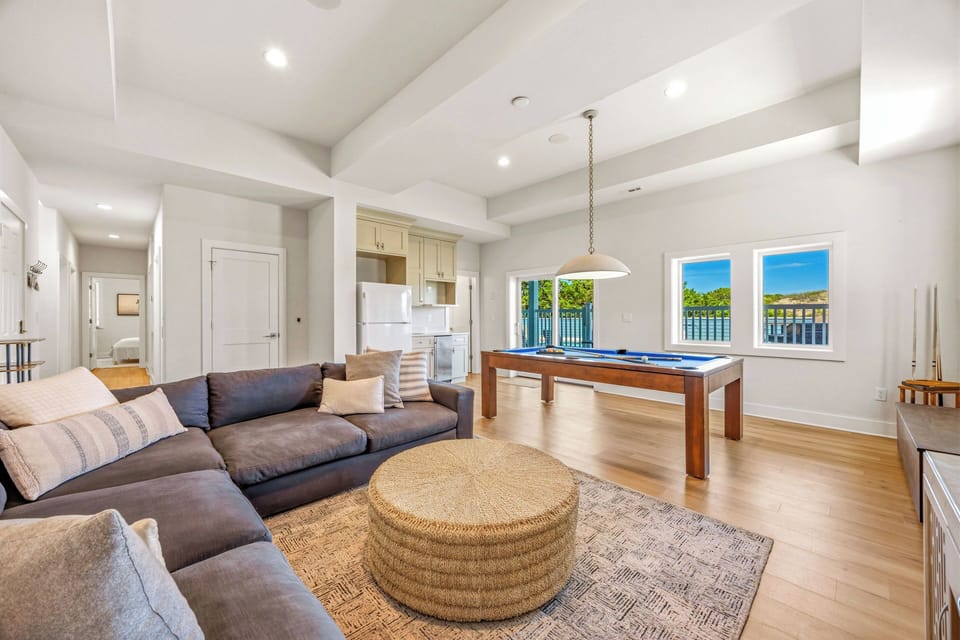 Gather in your sun-drenched living space, where plush seating invites conversation, a sleek pool table promises friendly competition, and waterfront views frame every moment.