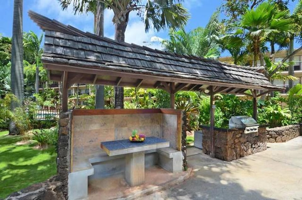 Gas barbecue area with picnic tables surrounded by tropical flora and fauna. 
