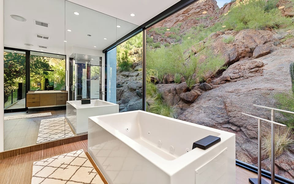 Spa-like bath with soaking tub, floor-to-ceiling glass & Camelback views.
