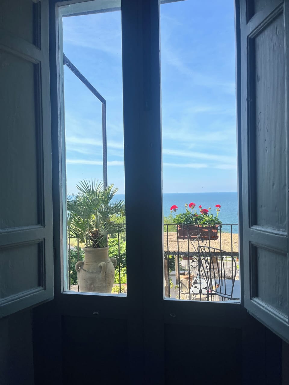 Sea view and shutters lead to large balcony with red geraniums and lemon trees