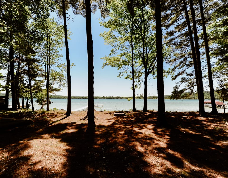 View of Little Traverse Lake from the cottage deck shaded by tall one trees.