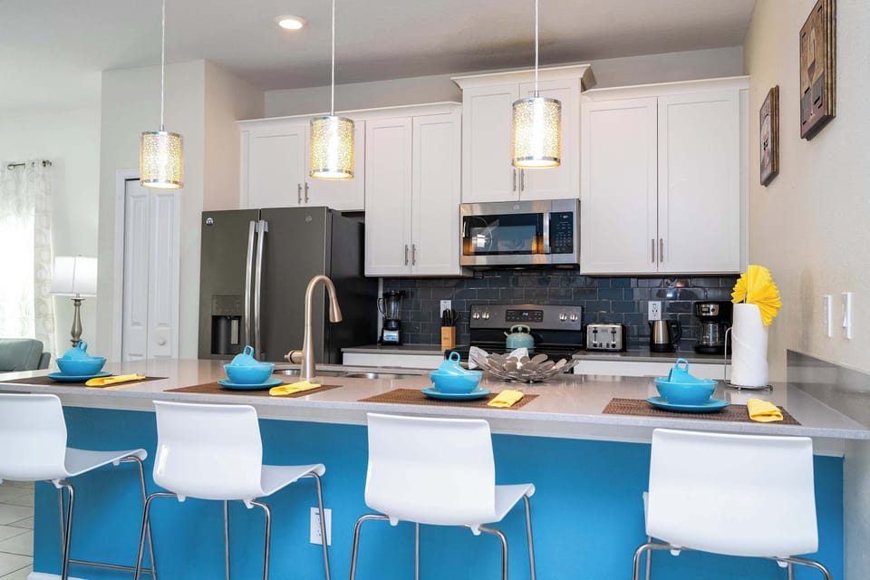 Enjoy your morning coffee at this sleek breakfast bar! The kitchen's modern white cabinetry and bright blue island create a cheerful, inviting vibe.