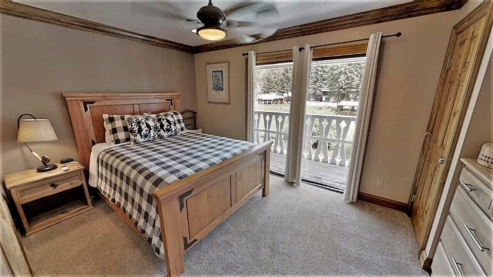 Your cozy bedroom features rustic wood furnishings, a ceiling fan for comfort, and balcony doors opening to serene snow-dusted pines—inviting restful mountain mornings.