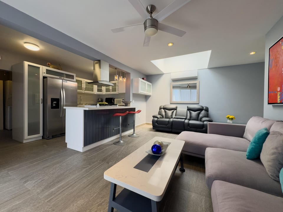 Living area features a gray sectional, black leather loveseat, and a marble-top coffee table beneath a skylight.