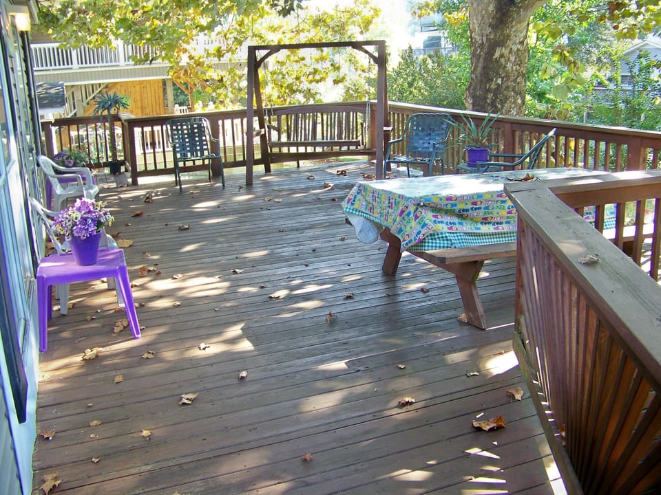large deck with swing, table and chairs under a large shade tree.