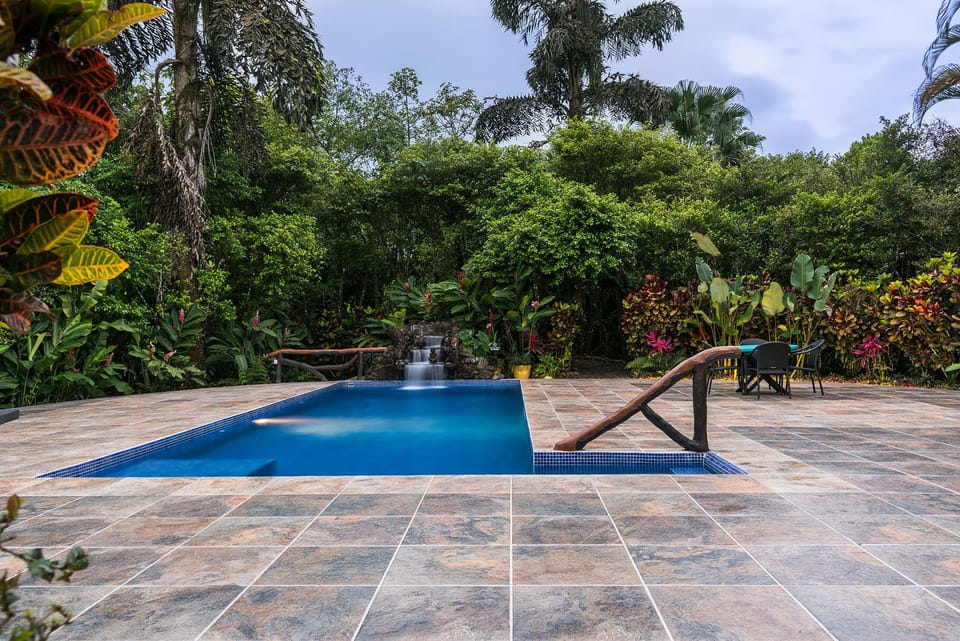 Swimming pool with waterfall and wood-designed railing.