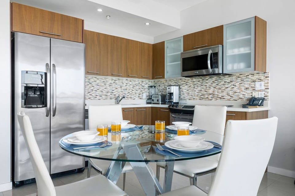 Your fully equipped kitchen awaits with stainless appliances, sleek cabinetry, and a chic glass dining table set for four—perfect for morning coffee or preparing meals during your stay.