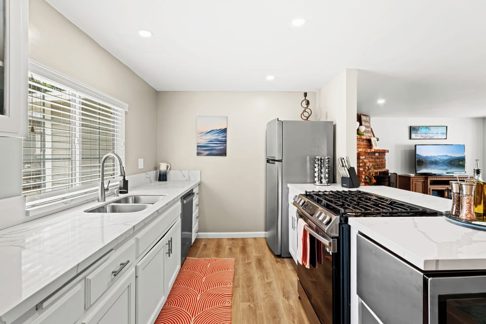 Enjoy cooking in this bright, modern kitchen with sleek white cabinetry, quartz countertops, and bar seating for casual meals or morning coffee. Fully stocked for all your culinary needs.