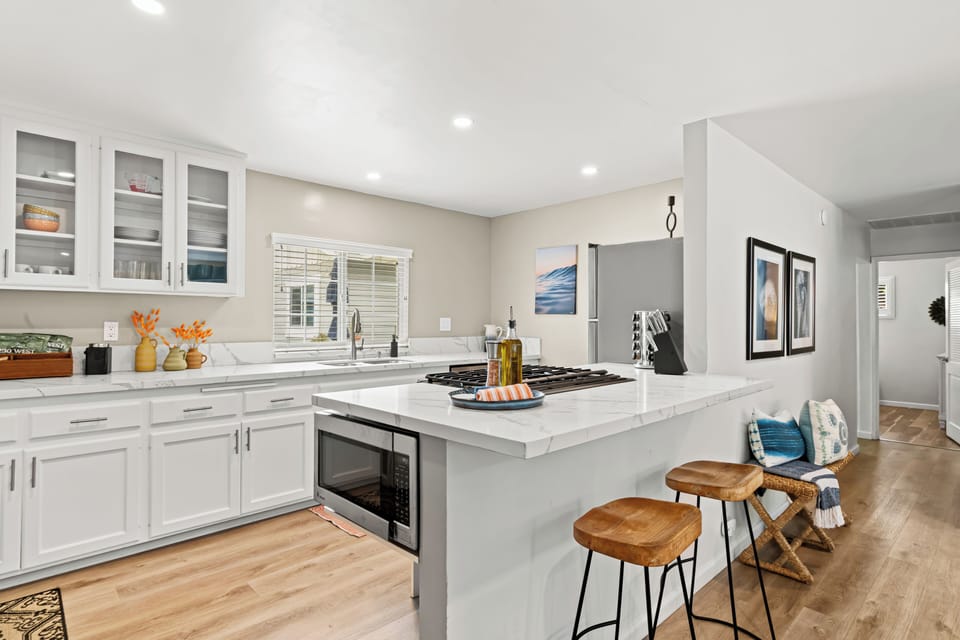 Enjoy cooking in this bright, modern kitchen with sleek white cabinetry, quartz countertops, and bar seating for casual meals or morning coffee. Fully stocked for all your culinary needs.