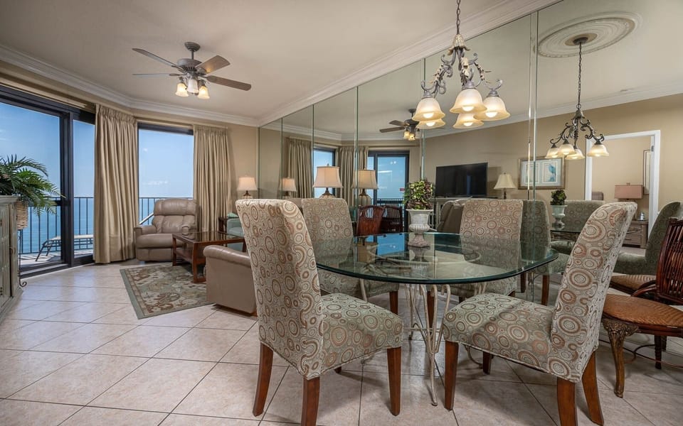 Dining area features a glass table with chairs, overlooking the balcony and the serene gulf view through large windows