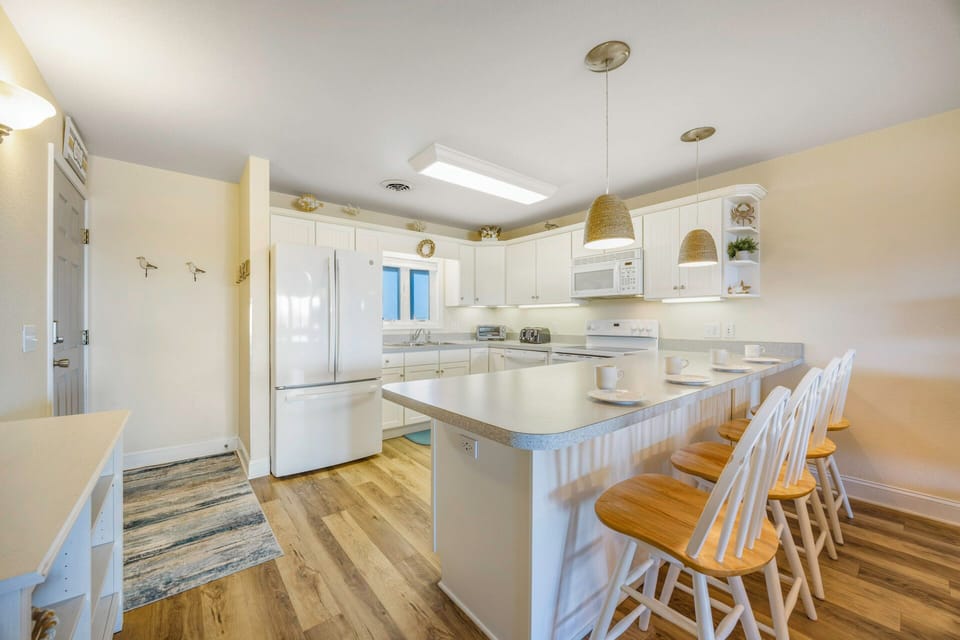 Your spacious kitchen invites you to gather around the breakfast bar, where morning coffee feels extra special with crisp white cabinets and warm wood floors.