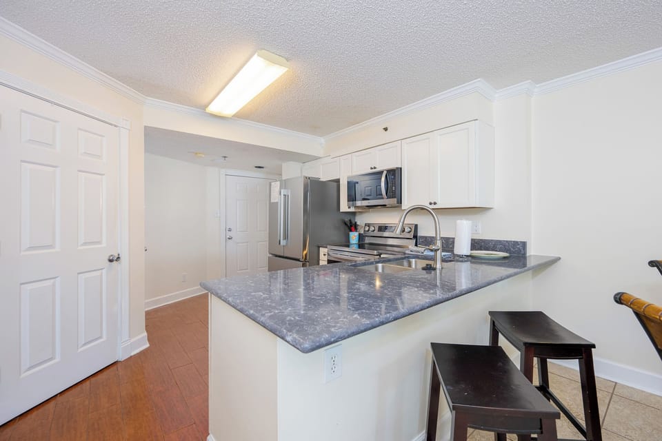 This kitchen features white cabinetry, essential appliances, and a breakfast bar with seating, perfect for casual dining