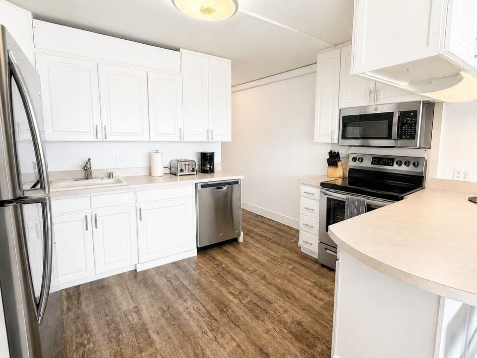 A fully equipped kitchen with crisp white cabinetry, stainless appliances, and a breakfast bar with seating