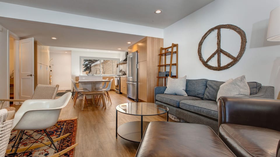 Unwind in our chic open-concept living area, featuring a comfortable sofa, modern kitchen access, and a unique peace sign. Perfect for a relaxing stay.
