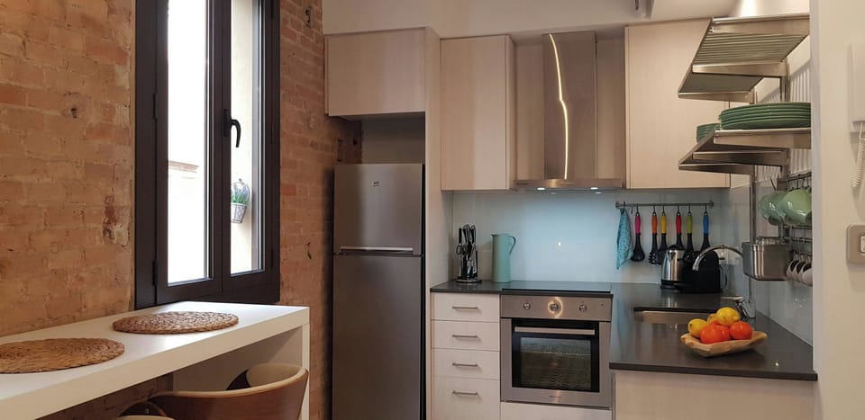 The apartment's kitchen is a modern and well-equipped space with sleek stainless steel appliances and a bright, airy feel. The exposed brick wall adds a touch of industrial charm, while the window provides natural light. The kitchen is fully equipped with