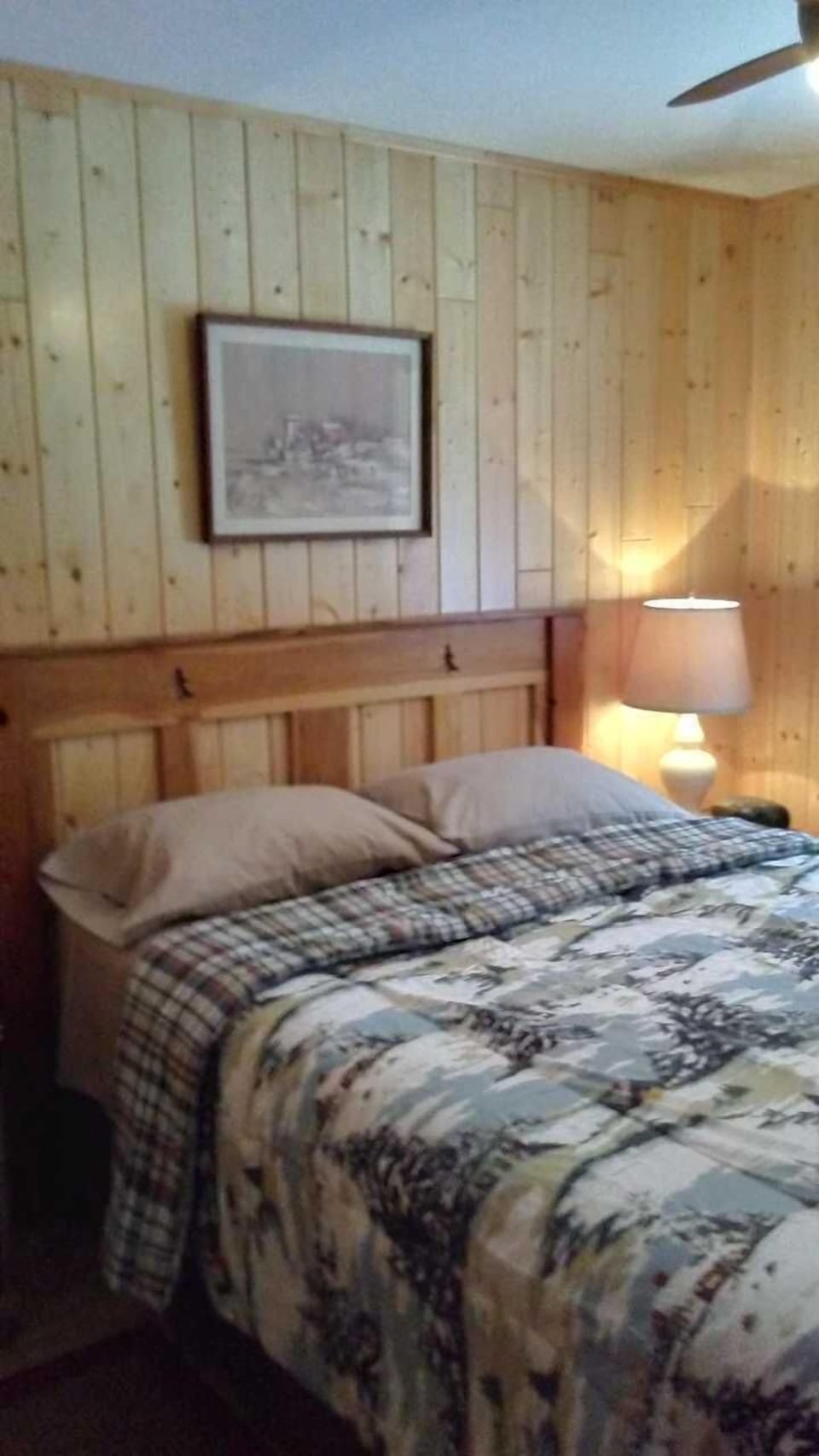Master bedroom with a queen size bed, knotty pine walls, and a ceiling fan.