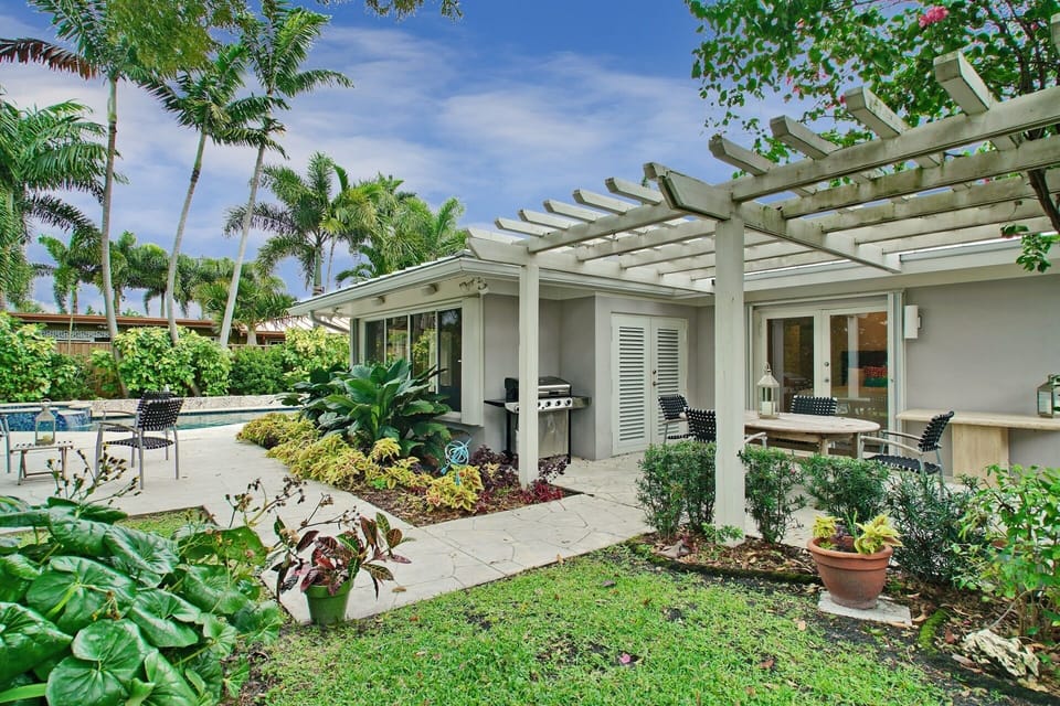 Dining al fresco under the pergola with grill, lush landscaping and mood light